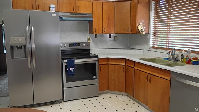 Kitchen with appliances with stainless steel finishes, light countertops, brown cabinets, and under cabinet range hood | Image 16