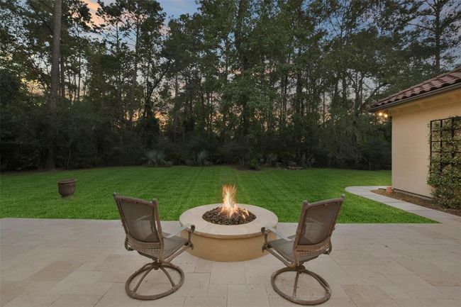 Gather around the fire pit while enjoying this gorgeous view of a lush, green backyard bordered by tall, mature trees. Perfect for tranquil evenings and intimate gatherings. | Image 40