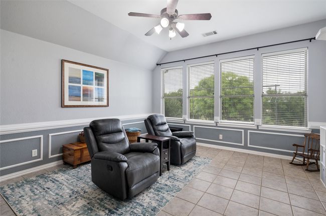 Sitting room with light tile patterned floors, lofted ceiling, a wainscoted wall, and a ceiling fan | Image 7