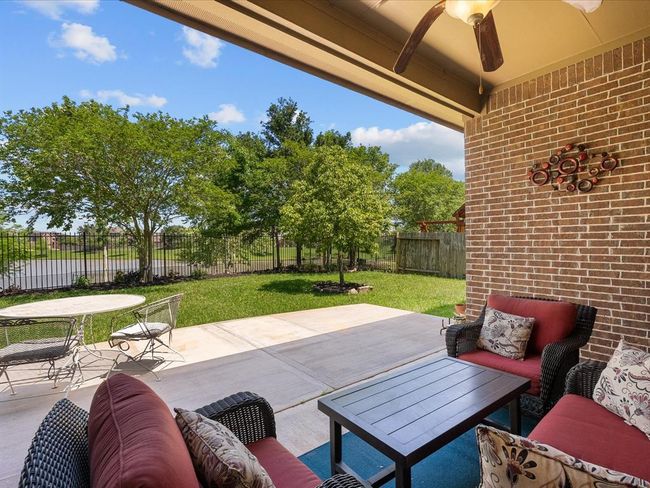 This photo showcases a charming patio with comfortable seating and a ceiling fan, overlooking a lush, fenced backyard. Ideal for outdoor relaxation and entertaining, it offers a serene view of greenery and open skies. | Image 46