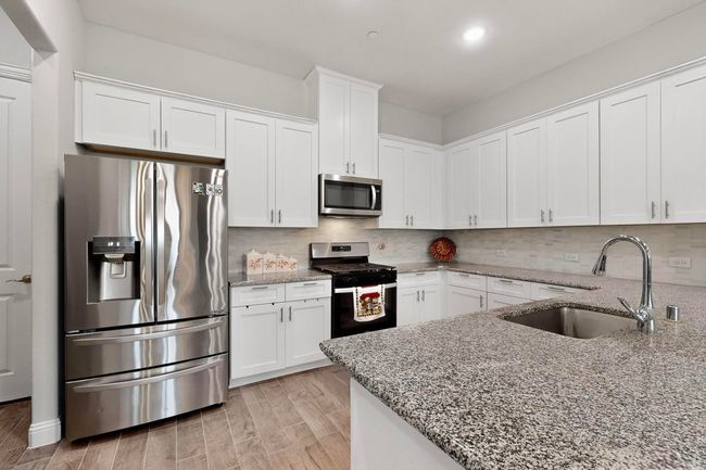 Kitchen featuring stainless steel appliances, white cabinetry, light stone countertops, backsplash, and recessed lighting | Image 10