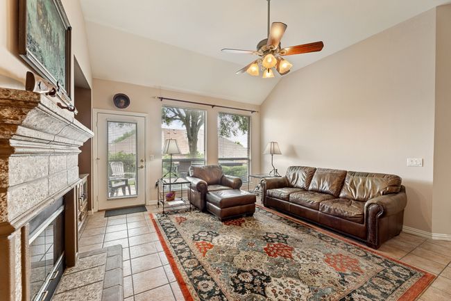 Living area with vaulted ceiling, ceiling fan, light tile patterned floors, a stone fireplace, and baseboards | Image 11