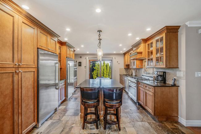 Kitchen with high end appliances, a sink, a kitchen island, brown cabinetry, and stone tile flooring | Image 5