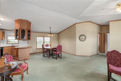 Carpeted dining space with ceiling fan with notable chandelier, a healthy amount of sunlight, a textured ceiling, and crown molding. | Image 3