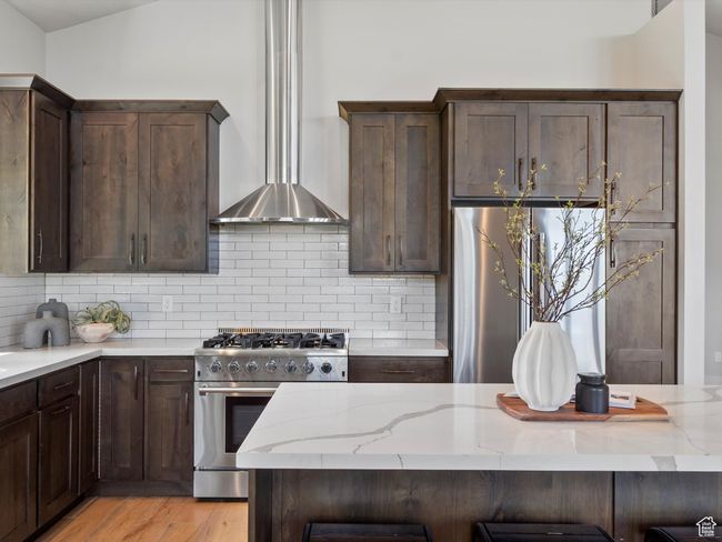 Kitchen with appliances with stainless steel finishes, wall chimney range hood, light stone countertops, tasteful backsplash, and dark brown cabinets | Image 17