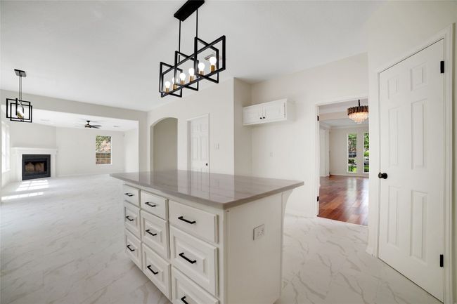 Kitchen with light marble finish floors, a fireplace, open floor plan, arched walkways, and ceiling fan | Image 5