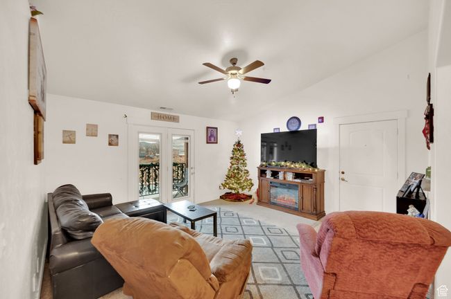 Living area featuring vaulted ceiling, ceiling fan, light carpet, a glass covered fireplace, and french doors | Image 6