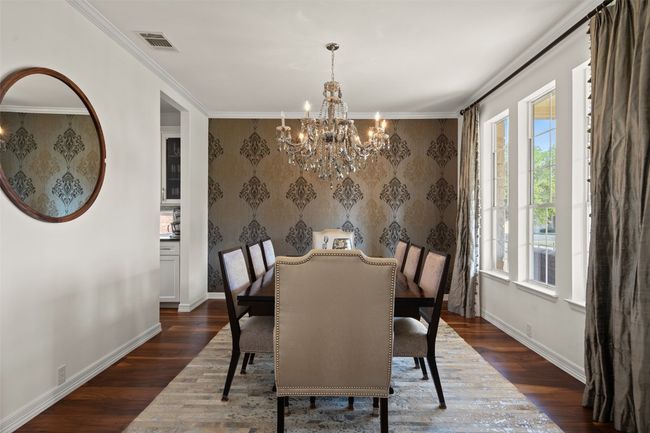 Dining room with wallpapered walls, a notable chandelier, dark wood-type flooring, and visible vents | Image 10