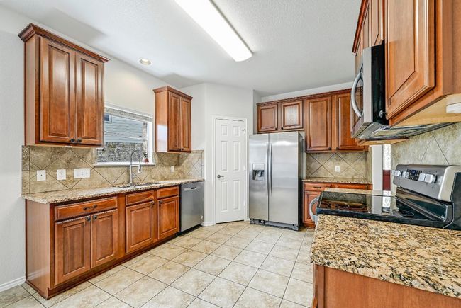 Kitchen featuring appliances with stainless steel finishes, light tile patterned floors, brown cabinetry, and tasteful backsplash | Image 6