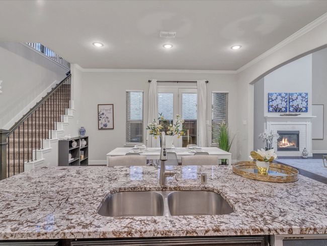 Kitchen featuring open floor plan, recessed lighting, a glass covered fireplace, crown molding, and light stone counters | Image 13