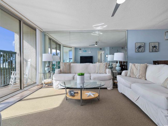 Living room with a textured ceiling, a wall of windows, carpet, and ceiling fan | Image 5