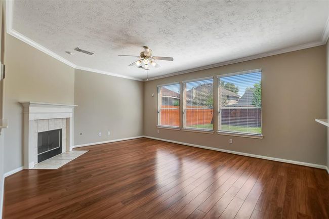 Spacious living room with hardwood floors, large windows offering ample natural light, a ceiling fan, and a cozy fireplace for comfort. | Image 12