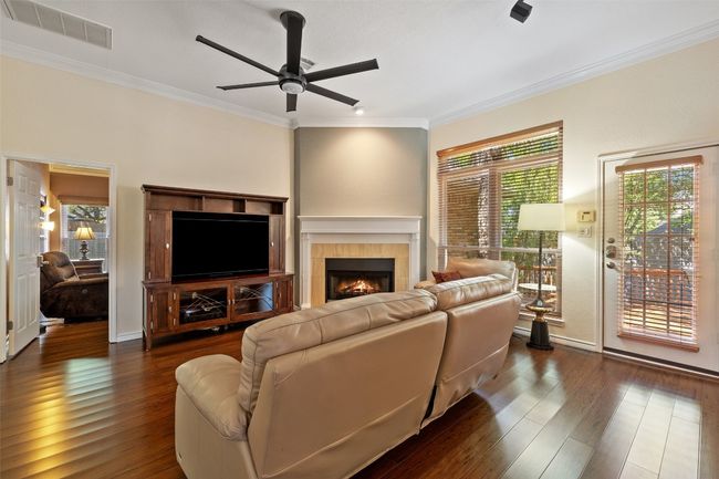 Living room featuring plenty of natural light, ceiling fan, a tiled fireplace, crown molding, and dark wood-style floors | Image 8