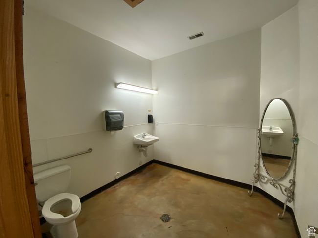 Half bathroom with unfinished concrete flooring, toilet, baseboards, and visible vents | Image 26