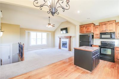 Kitchen with lofted ceiling, a kitchen island, black appliances, a fireplace, and ceiling fan with notable chandelier | Image 3