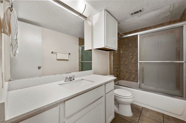 Full bath featuring vanity, a textured ceiling, enclosed tub / shower combo, and tile patterned floors | Image 11