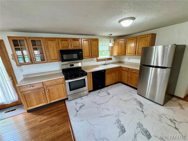 Kitchen featuring black appliances, brown cabinets, a textured ceiling, light countertops, and a sink | Image 21