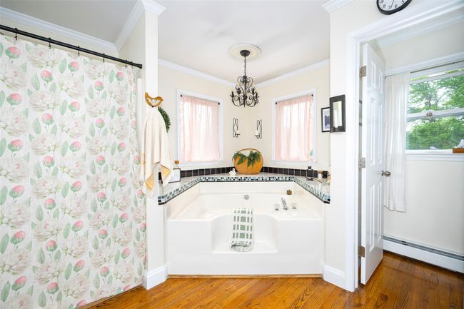 Bathroom with a chandelier, a garden tub, baseboard heating, wood finished floors, and crown molding | Image 17