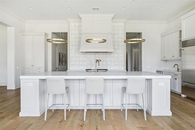 This stunning kitchen features a one-of-a-kind island with a spacious breakfast bar, offering seating for four. Topped with exquisite Opal White marble, the island is complemented by a sleek Blanco Specialty sink and a luxe gold Brizo faucet. Overhead, designer pendant lighting adds a touch of sophistication, enhancing the kitchen’s elegant and functional design. | Image 12