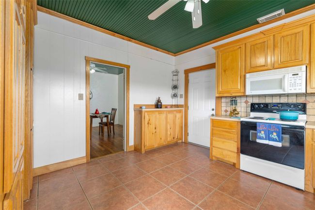 Kitchen with white microwave, electric range, light countertops, decorative backsplash, and ceiling fan | Image 16