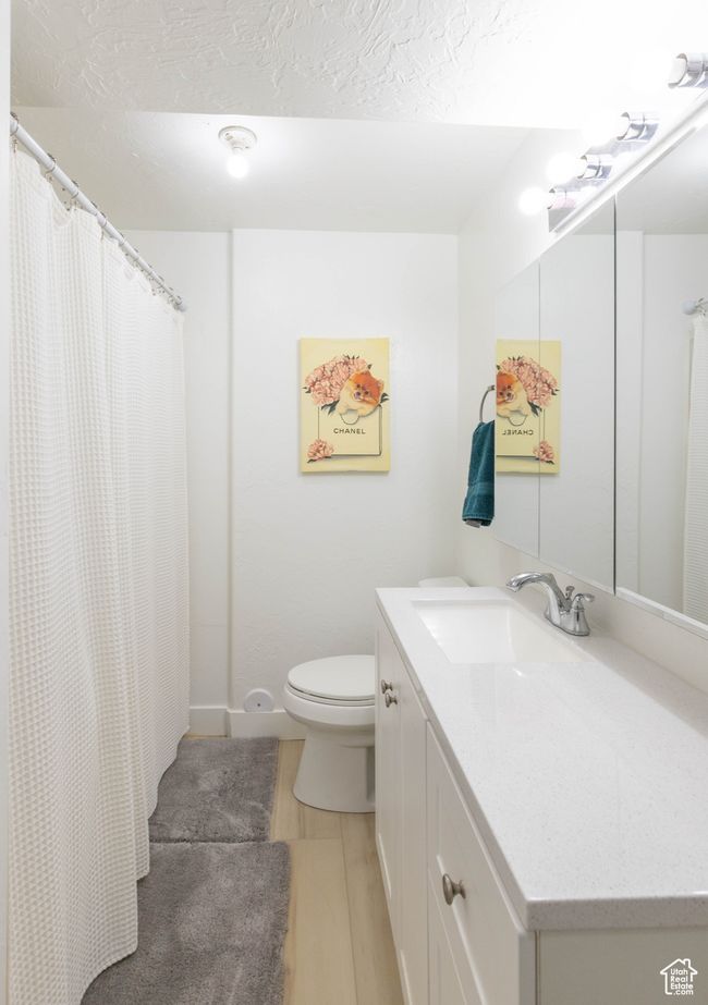Bathroom featuring toilet, vanity, a shower with curtain, a textured ceiling, and wood finished floors | Image 8
