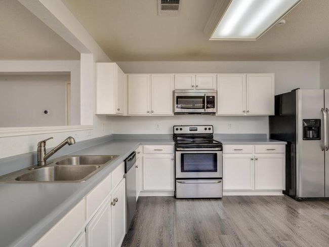 Kitchen featuring appliances with stainless steel finishes, white cabinets, luxury vinyl wood-look flooring, and light countertops. | Image 12