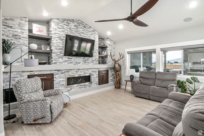 Living area with ceiling fan, a stone fireplace, lofted ceiling, wood finished floors, and recessed lighting | Image 14