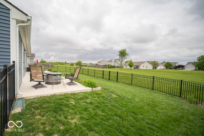 view of rear yard from the corner with a full concrete patio area across the rear of the home and a full black aluminum fence backing up to a large common area | Image 24
