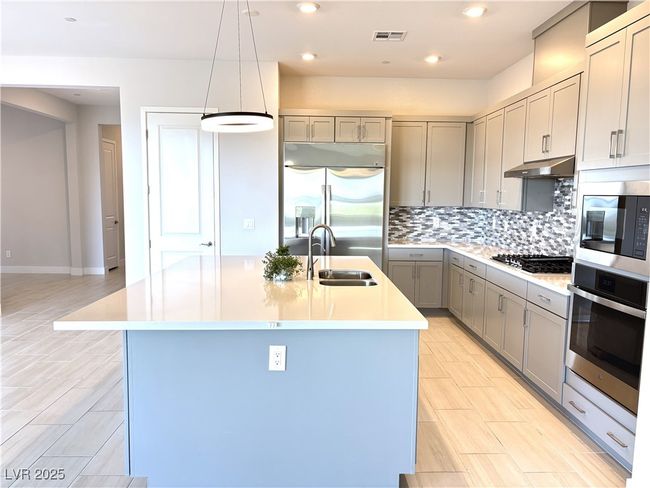 Kitchen with a sink, stainless steel appliances, decorative backsplash, visible vents, and gray cabinetry | Image 11