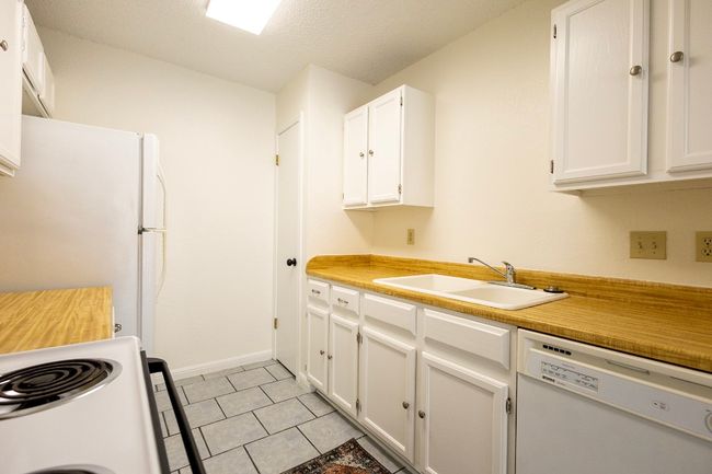 Kitchen featuring white appliances, a sink, white cabinetry, light countertops, and light tile patterned floors | Image 30