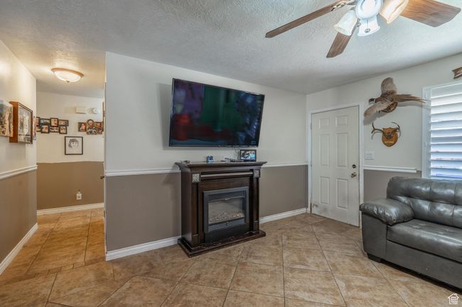 Living room with ceiling fan, a textured ceiling, a glass covered fireplace, and light tile patterned flooring | Image 17