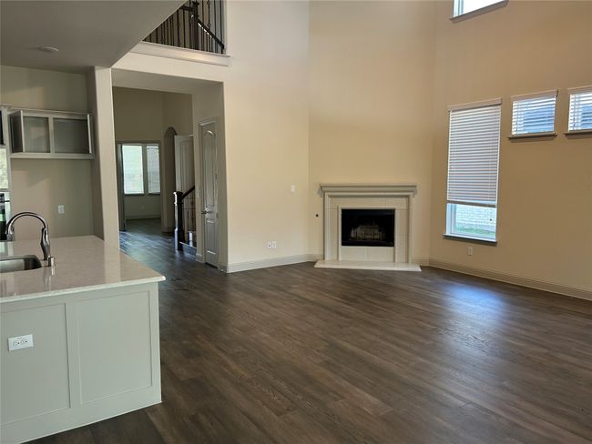 Unfurnished living room with a towering ceiling, a sink, dark wood-type flooring, a tiled fireplace, and baseboards | Image 16