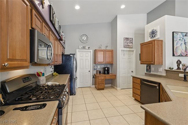 Kitchen featuring brown cabinets, built in desk, light countertops, light tile patterned flooring, and appliances with stainless steel finishes | Image 8