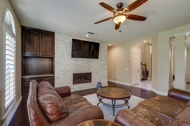 Living area featuring a ceiling fan, wood finished floors, a fireplace, and decorative columns | Image 10