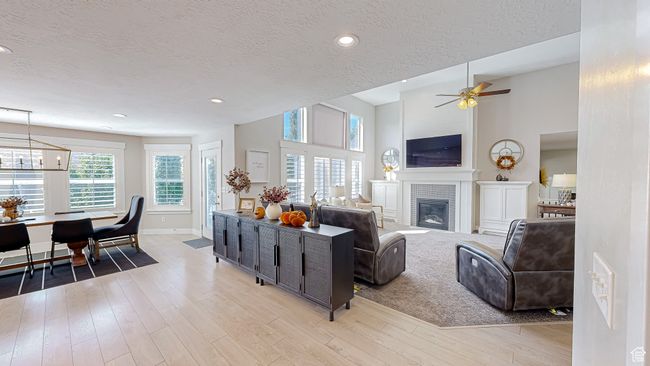 Living room with ceiling fan with notable chandelier, light wood-style floors, a glass covered fireplace, and a textured ceiling | Image 14