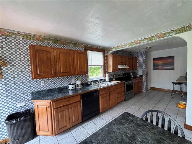 Kitchen with electric stove, black dishwasher, a sink, under cabinet range hood, and a textured ceiling | Image 6