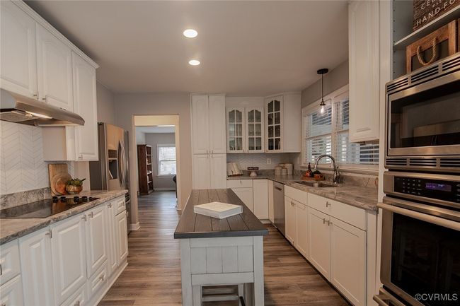 Kitchen with dark wood-style flooring, a sink, stainless steel appliances, glass insert cabinets, and under cabinet range hood | Image 12