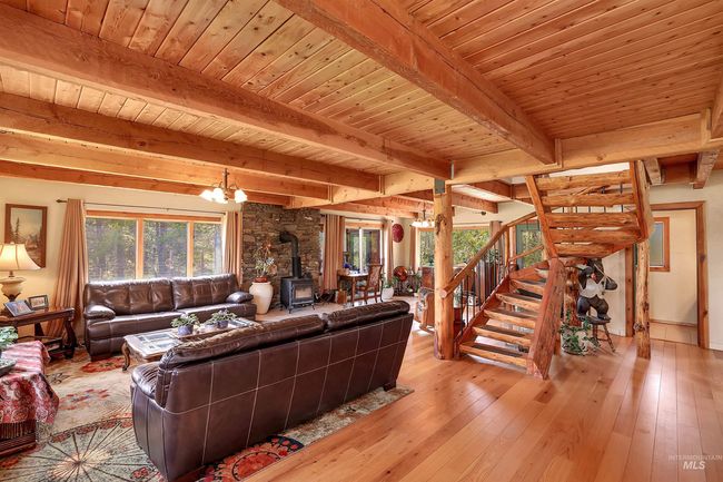 Living room with a wood stove, wood-type flooring, a chandelier, stairway, and a wood ceiling with exposed beams | Image 9