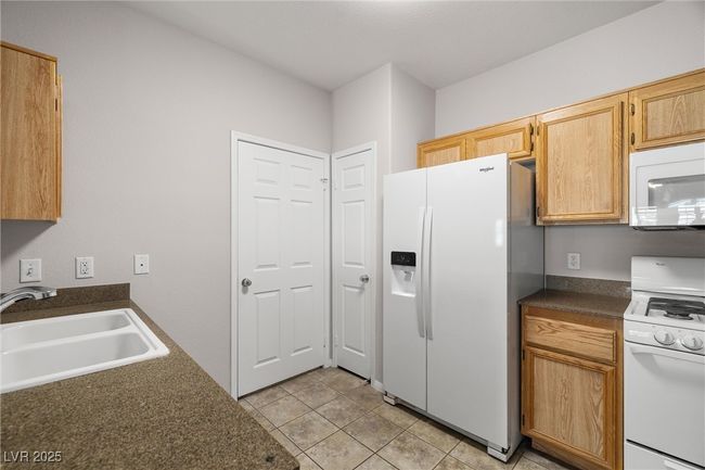 Kitchen with light tile patterned floors, dark countertops, a sink, and white appliances | Image 18