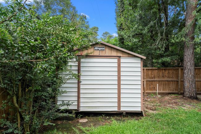 A quaint backyard storage shed with a white and brown exterior, surrounded by lush greenery and enclosed by a wooden fence, perfect for extra storage. Located behind the detached garage. | Image 44