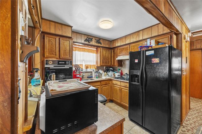 Kitchen featuring black appliances, light tile patterned floors, brown cabinets, and light countertops | Image 12
