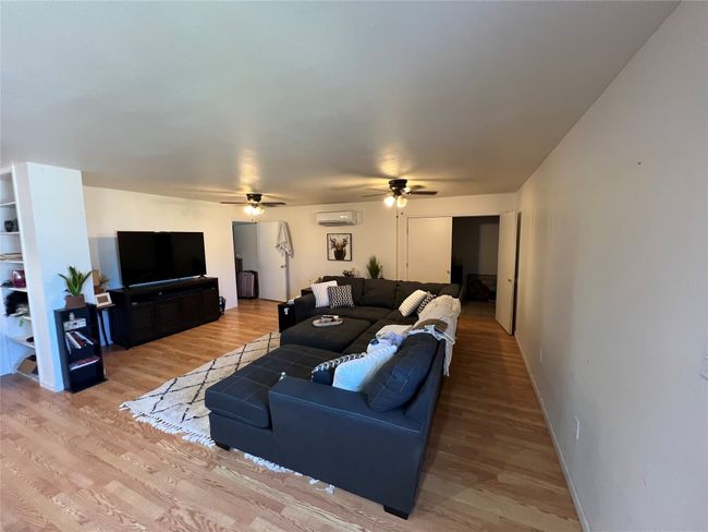 Living room with ceiling fan, an AC wall unit, light wood finished floors, and baseboards | Image 11