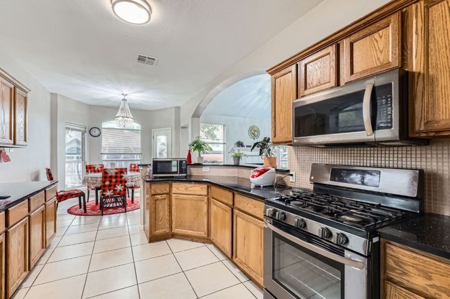 Kitchen featuring stainless steel appliances, decorative backsplash, arched walkways, light tile patterned floors, and dark stone countertops | Image 10