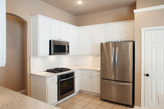 Kitchen with stainless steel appliances, white cabinetry, backsplash, light stone counters, and arched walkways | Image 5