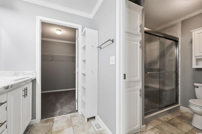 Bathroom with a textured ceiling, toilet, a stall shower, a walk in closet, and vanity | Image 20