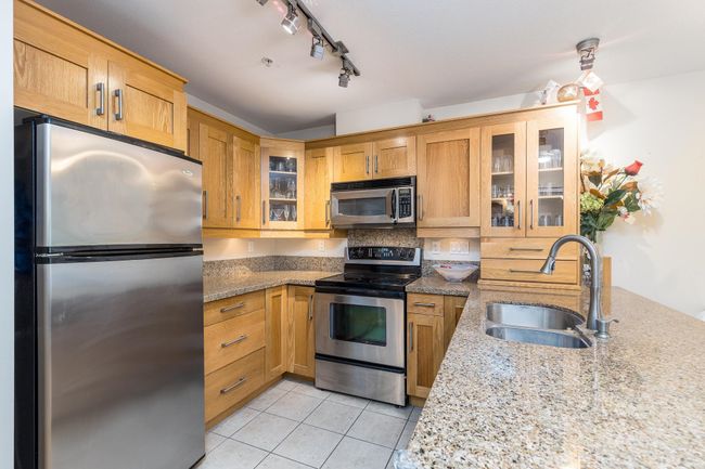 Kitchen with light tile patterned floors, light stone countertops, stainless steel appliances, and a sink | Image 6