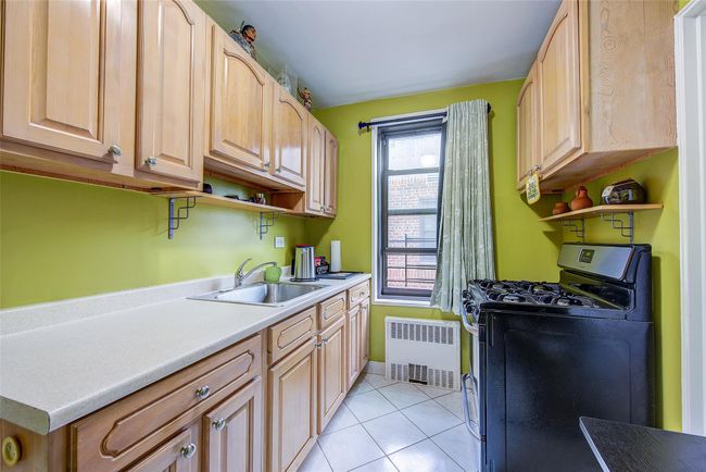 Kitchen featuring range with gas stovetop, radiator heating unit, open shelves, and light brown cabinetry | Image 13