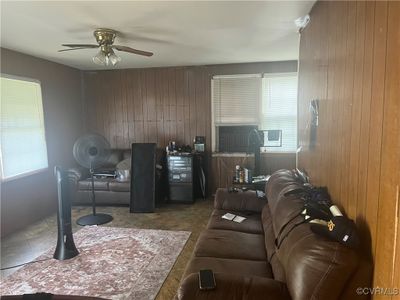 Living room with wood walls, cooling unit, tile patterned flooring, and ceiling fan | Image 3