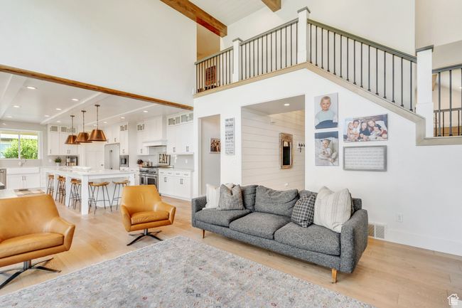 Living area featuring a towering ceiling, light wood finished floors, beamed ceiling, stairs, and recessed lighting | Image 17