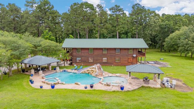 This photo showcases a charming two-story log cabin with a balcony, nestled in a lush green setting. It features a spacious patio area, an inviting pool, and a gazebo, perfect for outdoor relaxation and entertaining. Featuring waterfall slide and unwind in the nearby hot tub. A covered outdoor seating area is perfect for relaxation and entertaining. | Image 8